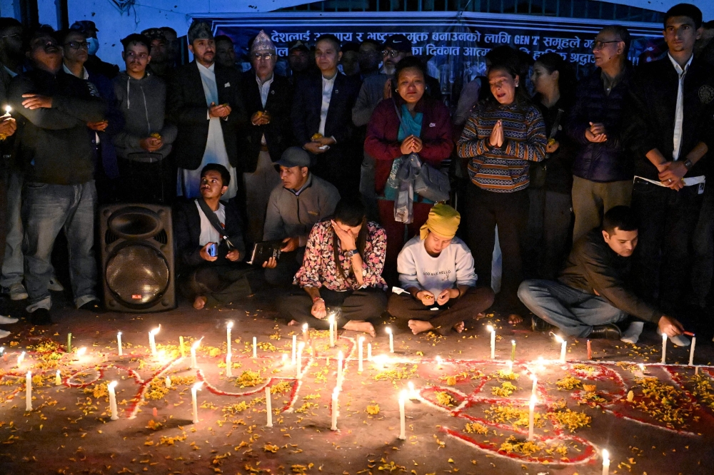Family members of those killed in September anti-corruption protests take part in a candlelight vigil in front of the fire-damaged parliament building in Kathmandu on November 9, 2025. (Photo by Prakash Mathema / AFP)
